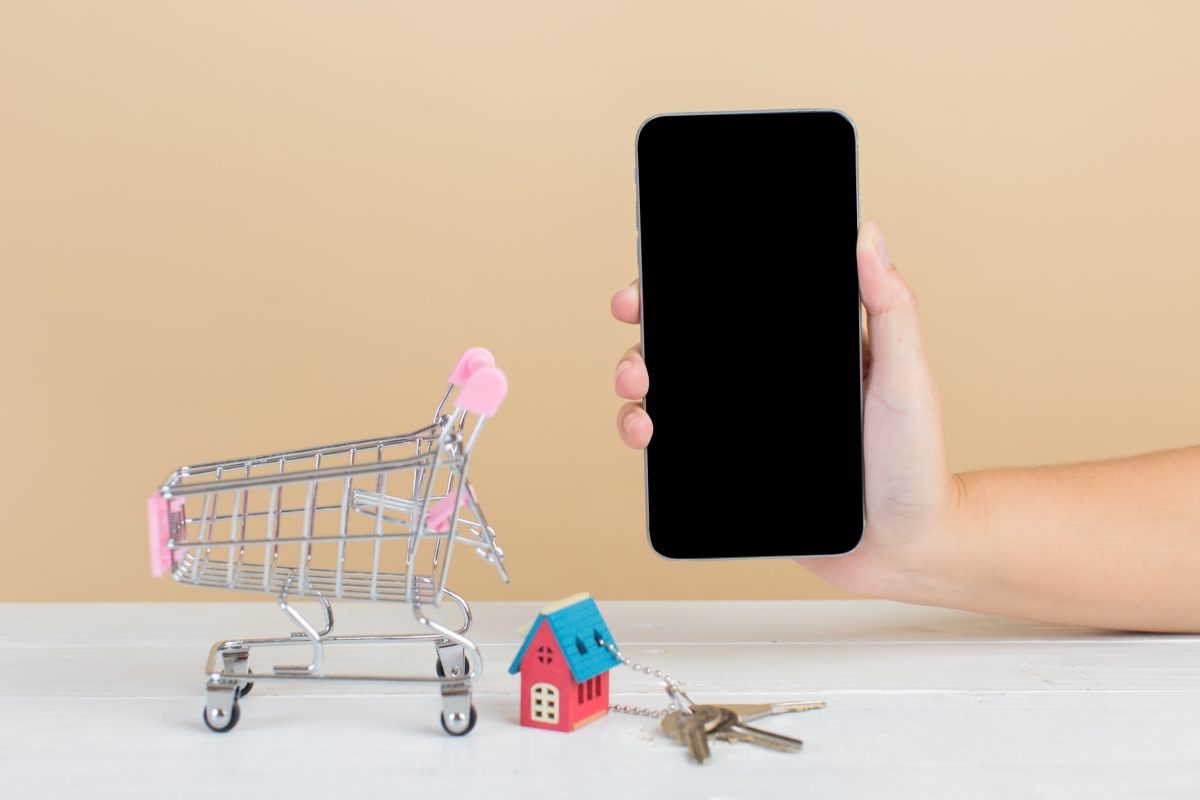 Imagem de celular, carrinho de compras e casa em miniatura para simular comprar um imóvel pela internet